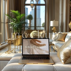 May include: A gold laptop computer with a white screen displaying the text "soul of thessaly est. 1961" on a white couch with a gold pillow.