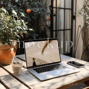 May include: A MacBook Pro mockup on a wooden table with a cup of coffee and a smartphone. The laptop screen displays the text "ANNABEE PHOTOGRAPHY". A potted plant is to the left. The image also includes the text "MACBOOK MOCKUP" and "PSD & JPG FILE".