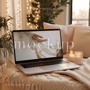 May include: A silver laptop computer with a white screen displaying the text "soul of the sky" and a photo of hands. The laptop is on a white and brown blanket with two candles in glass jars.