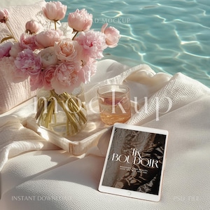 May include: A serene scene featuring a glass vase of pink peonies, a glass of rose-colored liquid, and a tablet with the text "Tix Boudoir". The items rest on a white surface near a pool of water, creating a tranquil aesthetic.