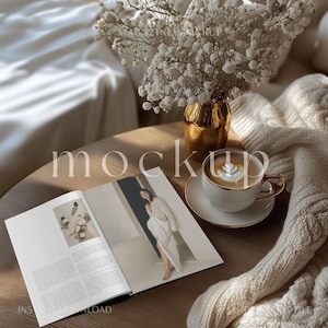 May include: A flat lay mockup featuring a magazine with a woman in a white dress on the cover, a cup of coffee with latte art, a vase with white flowers, and a white knitted blanket.
