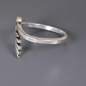Pu&ograve; includere: Un anello argentato con un design decorativo a forma di cuore. L'anello ha una fascia liscia e un elemento a cuore dettagliato e strutturato. L'anello &egrave; mostrato su uno sfondo grigio.