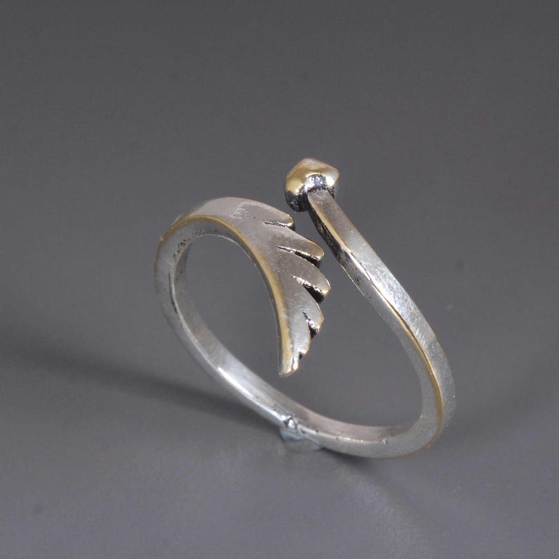 Pu&ograve; includere: Un anello argentato con un design a foglia e dettagli dorati. L'anello presenta un design aperto con un piccolo dettaglio dorato a forma di cuore nella parte superiore. Il dettaglio della foglia si curva attorno al dito.