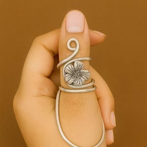 May include: A silver ring featuring a floral design. The ring wraps around the finger with a flower at the centre and a swirl at the top. A unique piece of jewellery.