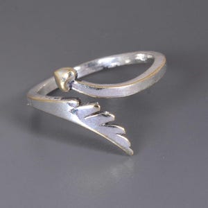 Pu&ograve; includere: Anello color argento con un accento a forma di cuore color oro e un design a forma di ala. L'anello ha un gambo diviso e una finitura lucida. Il dettaglio dell'ala &egrave; su un lato dell'anello, aggiungendo un tocco unico al gioiello.