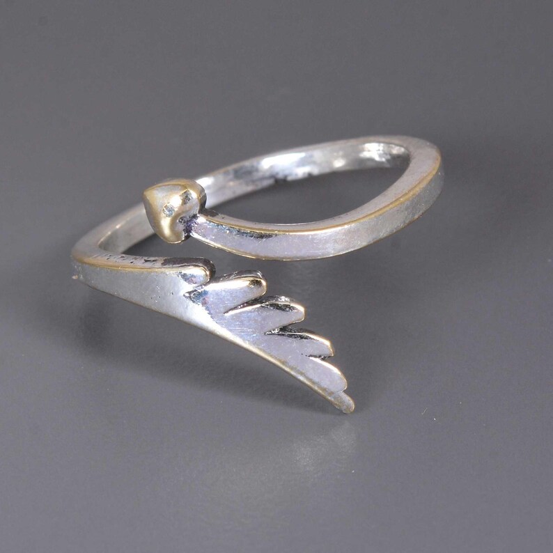 Pu&ograve; includere: Anello color argento con un accento a forma di cuore color oro e un design a forma di ala. L'anello ha un gambo diviso e una finitura lucida. Il dettaglio dell'ala &egrave; su un lato dell'anello, aggiungendo un tocco unico al gioiello.