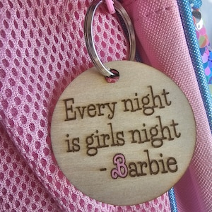 Puede incluir: Un llavero redondo de madera con el texto "Every night is girls night - Barbie" en letras negras. El llavero está unido a un anillo de llave plateado.