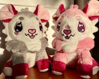 May include: Two plush toys, one grey and white with pink accents and the other pink and white with grey accents. Both have large eyes, a heart-shaped nose, and a smiling mouth.