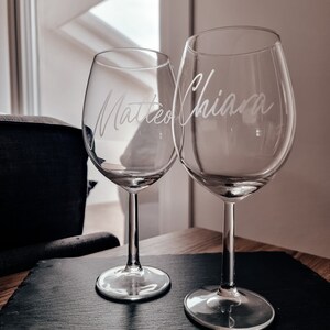 Può includere: Due bicchieri da vino in vetro trasparente con i nomi "Matteo" e "Chiara" incisi su di essi. I bicchieri sono su un vassoio da portata in ardesia nera.