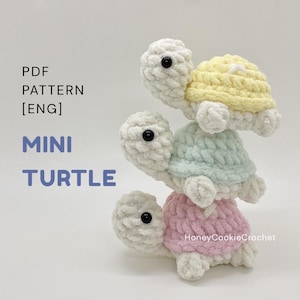 May include: Three stacked crochet turtle toys with white heads and limbs, featuring shells in pastel yellow, mint green, and light pink. The text reads PDF PATTERN [ENG] MINI TURTLE and HoneyCookieCrochet. The turtles have black plastic eyes.