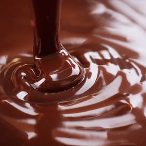 May include: Close-up of rich, dark brown chocolate being poured into a bowl, creating swirls and ripples on the surface.