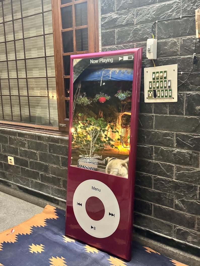 May include: A large, magenta, rectangular display screen shaped like a classic digital music player. The screen shows a Now Playing interface with a garden scene and the text Find Yourself. Below the screen is a white circular control wheel.