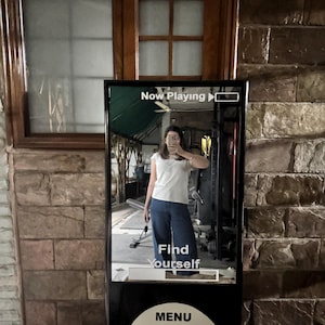 May include: A tall, rectangular mirror designed to resemble a vintage digital music player. The screen displays the text "Now Playing" at the top and "Find Yourself" in the center, with a circular control interface featuring a menu button.