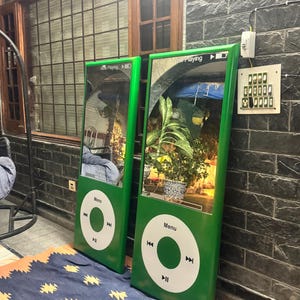 May include: Two tall, rectangular green mirrors designed to resemble classic digital music players. Each mirror features a white circular control interface with a Menu button and playback icons, plus a Now Playing display at the top of the glass.
