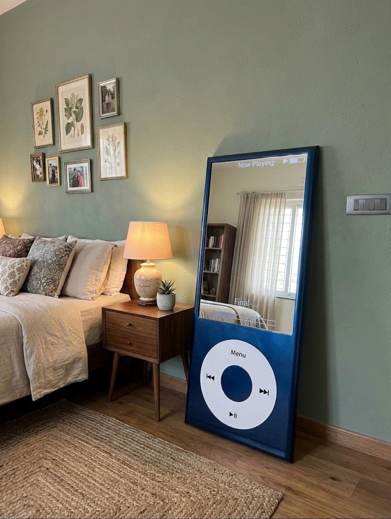 May include: A tall, rectangular floor mirror designed to resemble a classic digital music player. The frame is dark blue with a large white circular control wheel at the bottom featuring the text Menu and playback icons. The screen area is reflective.