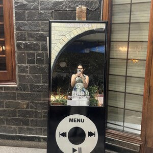 May include: A tall, rectangular black mirror designed to resemble a vintage portable music player. The top section features a reflective surface with the text "NOW PLAYING" and "FIND YOURSELF." The bottom section displays a large white circular control interface with "MENU," skip, and play/pause symbols.