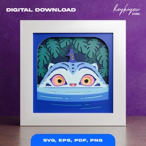 Può includere: Una stampa artistica digitale incorniciata raffigurante una creatura blu e bianca stravagante con grandi occhi gialli, su uno sfondo di foglie verdi. L'opera d'arte è incorniciata in una cornice quadrata bianca con il testo "DIGITAL DOWNLOAD" in alto e "SVG, EPS, PDF, PNG" in basso.