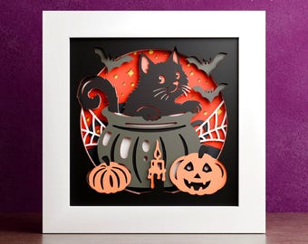 May include: A Halloween-themed paper cut design featuring a black cat in a cauldron, pumpkins, bats, and a spiderweb. The design is set against a red and orange background, with the words "DIGITAL DOWNLOAD" at the top. The image is framed in a white square.