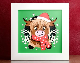 May include: A layered paper art piece featuring a cartoon Highland cow wearing a Santa hat and a red scarf with white stars. The artwork is set against a green background with white snowflakes and is framed in a white square. Text at the top reads "DIGITAL DOWNLOAD".