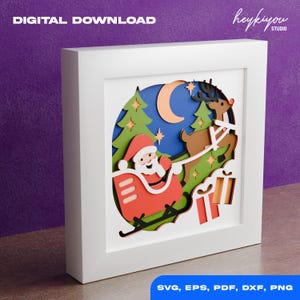 Peut inclure: Une œuvre d'art en papier sur le thème de Noël encadrée. Le Père Noël dans un traîneau rouge tiré par un renne, avec un croissant de lune et des étoiles en arrière-plan. Les mots "TÉLÉCHARGEMENT NUMÉRIQUE" et "SVG, EPS, PDF, DXF, PNG" sont visibles.