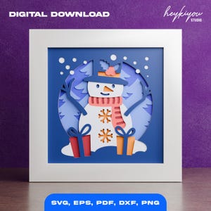 May include: A framed paper cut-out of a snowman with a blue hat, orange scarf, and snowflake details. The artwork includes two gift boxes and a snowy forest background. Text at the top reads "DIGITAL DOWNLOAD" and at the bottom "SVG, EPS, PDF, DXF, PNG".