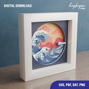 May include: A digital download of a paper cut design featuring a blue wave crashing against a pink and orange sunset. The design is in a circle shape and is perfect for creating a 3D paper art project. The file formats included are SVG, PDF, DXF, and PNG.
