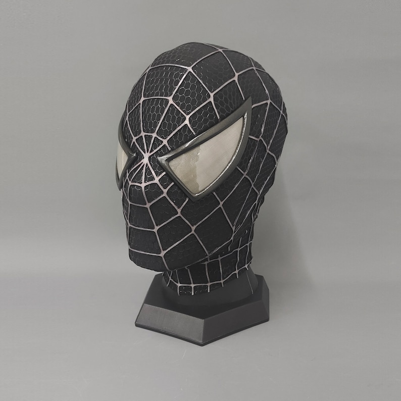 Puede incluir: M&aacute;scara de Spider-Man en blanco y negro con una base negra. La m&aacute;scara tiene un dise&ntilde;o de telara&ntilde;a y ojos blancos.