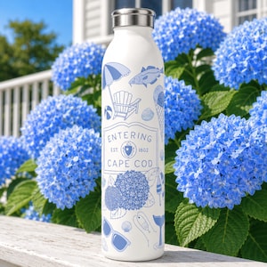 Könnte beinhalten: Eine weiße Edelstahl-Wasserflasche mit silbernem Verschluss, verziert mit blauen Strichzeichnungen von Strandartikeln, Hortensien und dem Text Entering Cape Cod Est. 1602, der mittig auf der Vorderseite des zylindrischen Behälters steht.