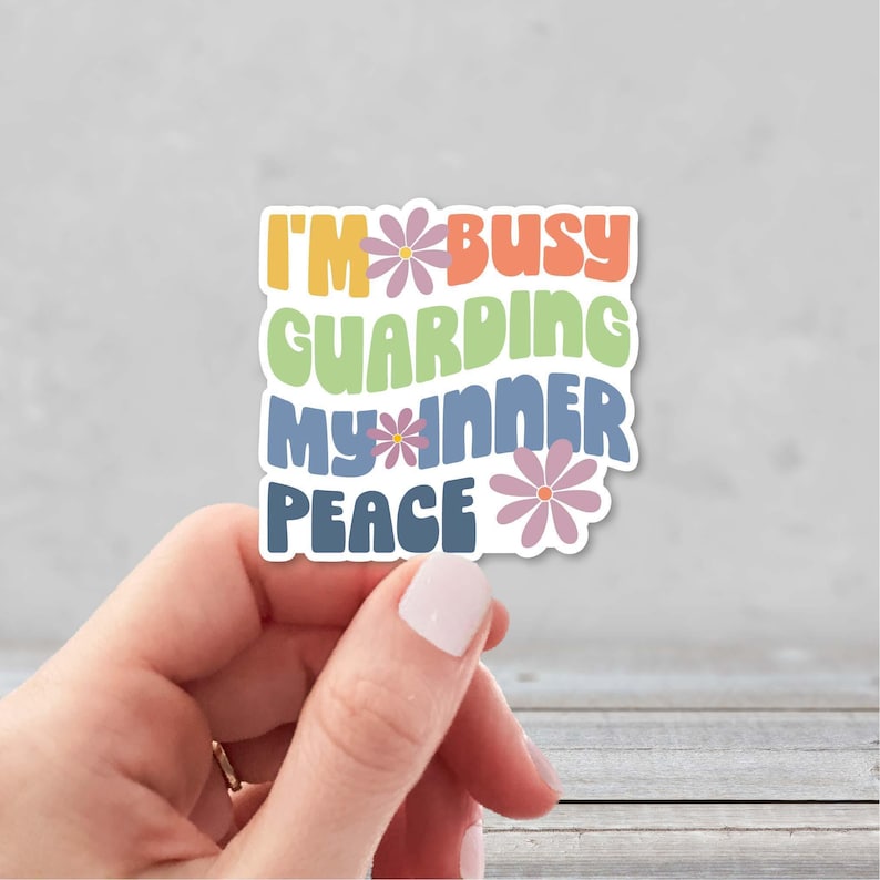 Hand holding a colorful sticker in a retro font that says I'm busy guarding my inner peace