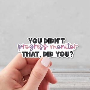 May include: A white sticker with the text "YOU DIDN'T progress monitor THAT, DID YOU?" in black, purple, and pink. The sticker is held by a hand with a light pink nail polish.