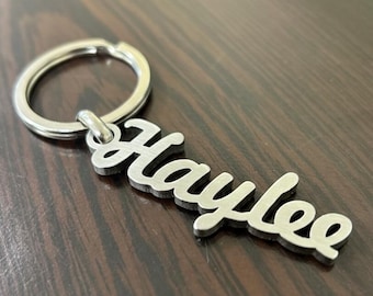 May include: A silver-colored keychain with the name "Haylee" in a cursive font. The keychain has a circular ring for attaching keys. The name is cut out of a metal plate.