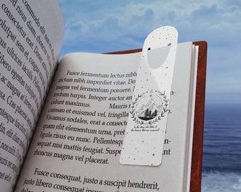 May include: A white bookmark with a black and white illustration of a mountain range and trees. The bookmark has the text "To the story who is written in the dreams that are remembered."