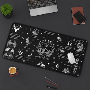 May include: Black rectangular desk mat with white illustrations and text. The design includes a deer head, moons, stars, and the text "Velaris City of Starlight". A computer mouse, laptop, and coffee cup are also visible.