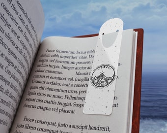 May include: A white bookmark with a black and white illustration of a mountain range, stars, and crescent moons. The text "To the stars who listen, no the dreams that are answered" is printed around the illustration.