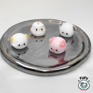 May include: Four small, handmade felt animal plushies on a silver tray. The plushies are a white chick with yellow accents, a white bear with yellow ears, a white panda with black ears, and a pink pig with pink ears.