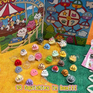 May include: A collection of colorful squishies in various shapes and colors, displayed with clear plastic containers. The image includes two illustrated boxes with cartoon characters and the text "24 Squishies in box!!!".