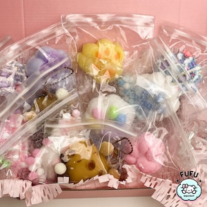 May include: Assortment of colorful squishy toys in clear plastic bags. The toys are in various shapes and sizes, including a paw print, a flower, and a heart. The bags are labeled with the word "Fufu Squishy".