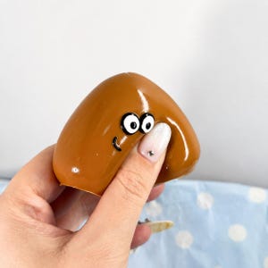 May include: A smooth, brown, arched object with a glossy finish featuring two large, white, circular eyes with black pupils and a small, curved black line representing a mouth, creating a simple, cartoon-like facial expression on its surface.