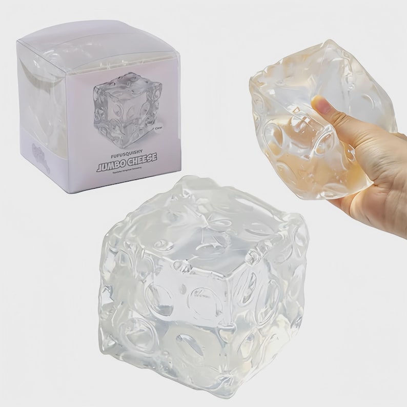 May include: A clear, squishy cube toy with a cheese-like design. The toy is shown in a clear plastic box and also being held by a hand. The text "FUFUSQUISHY JUMBO CHEESE" is printed on the box.