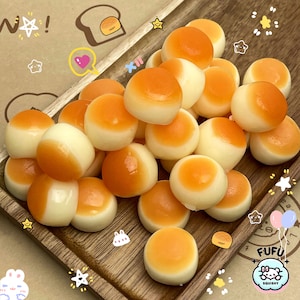 May include: A collection of 18 squishy, round, orange and white mochi squishies. The squishies are arranged on a wooden tray. The squishies are all different sizes and shapes.