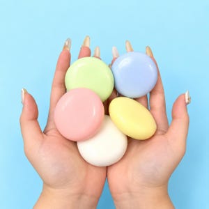May include: Five smooth, circular objects in pastel colors including light green, light blue, pink, yellow, and white. Each object has a glossy, solid finish and a rounded, disc-like shape, held together in a cluster against a light blue background.