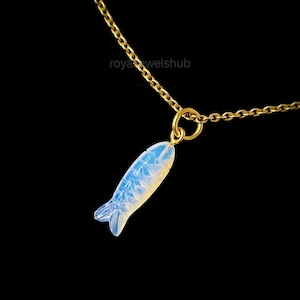 May include: A gold-colored chain necklace with a pendant shaped like a fish. The fish pendant is carved from a light blue and white opalescent material. The necklace is set against a black background.