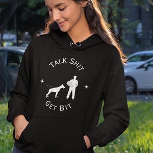 May include: Black hoodie with a white graphic that says "Talk Shit Get Bit" with a silhouette of a person holding a leash and a dog on a leash.