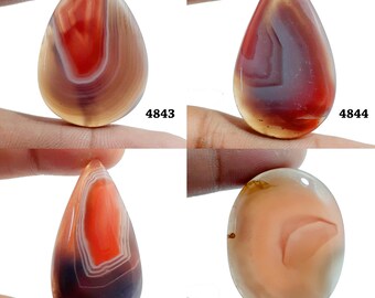 Könnte beinhalten: Vier Achat-Cabochons in Tropfen- und Ovalform mit roten, braunen und weißen Bändern. Die Cabochons sind mit 4843, 4844, 4845 und 4846 gekennzeichnet.