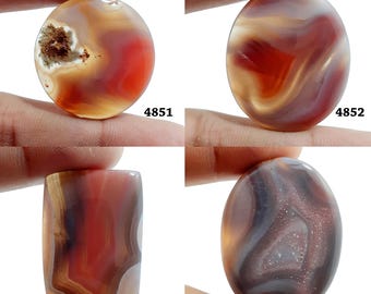 Könnte beinhalten: Vier Achat-Cabochons in verschiedenen Farben und Mustern, darunter Rot, Braun, Weiß und Grau. Die Cabochons sind oval und rechteckig geformt. Die Cabochons sind mit den Nummern 4851, 4852, 4853 und 4854 gekennzeichnet.