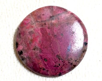 Puede incluir: Una piedra preciosa cabujón redonda, rosa y gris con una superficie pulida. La piedra tiene un patrón de remolino de rosa y gris.