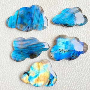 May include: Five cloud-shaped labradorite gemstones. The stones display a range of blues, with hints of yellow and grey. Each stone has a unique pattern and polished surface, ideal for jewellery making or collecting.