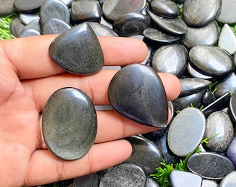 Könnte beinhalten: Eine Sammlung von schwarzen Obsidian-Cabochons in verschiedenen Formen und Größen. Die Steine haben eine schimmernde, irisierende Qualität.