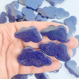 May include: Cloud-shaped blue sandstone stones with sparkling inclusions. The stones are a deep blue color and have a smooth, polished surface. The image shows several of these stones, some in focus and others blurred in the background. These stones are ideal for jewelry making or crafts.