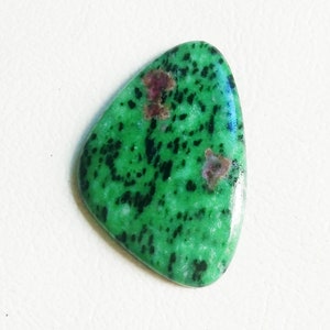 May include: A green gemstone with black and pink inclusions, cut into a triangular shape.